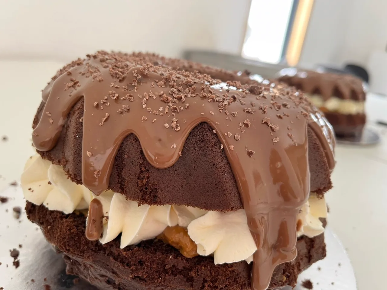 Close-up of a chocolate bundt cake with glossy chocolate glaze over whipped cream and caramel filling