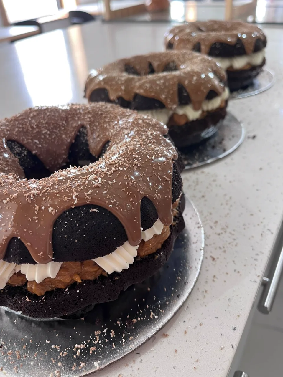 Three chocolate bundt cakes with dripping chocolate glaze lined up on the counter