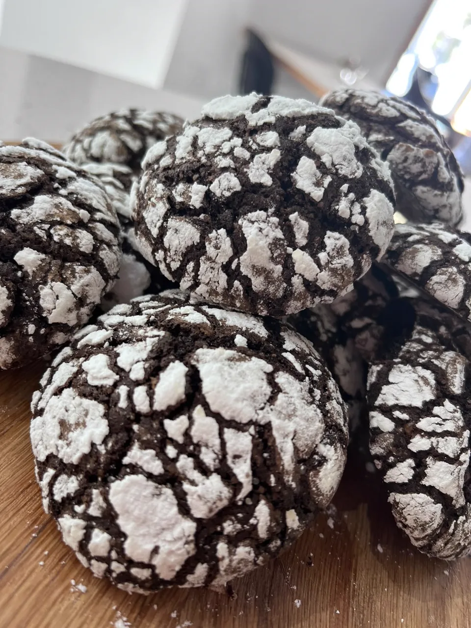 A pile of chocolate crinkle cookies dusted with icing sugar on a wooden board